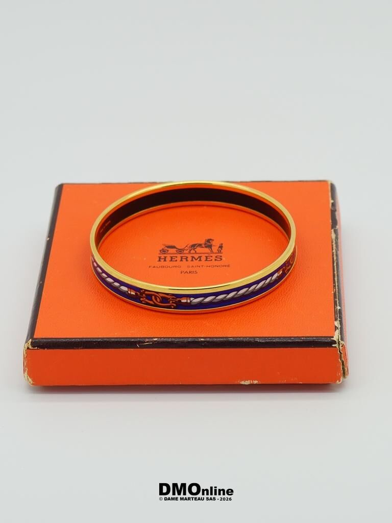 Orange Hermes box with a gold and blue enamel bangle resting atop it, the box showing wear on the edges.