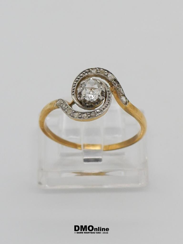 Gold ring with a central diamond and a curved, pave-set design on a clear display stand.