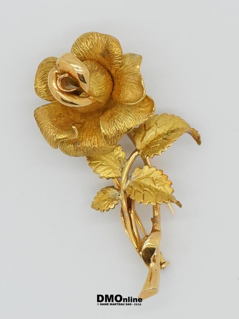 Gold-tone rose-shaped brooch with textured petals and curling leaves on a pale background