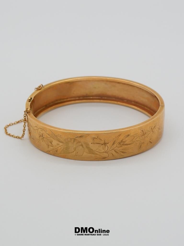 Gold-toned engraved bangle bracelet with a floral/leaf pattern and a small safety chain
