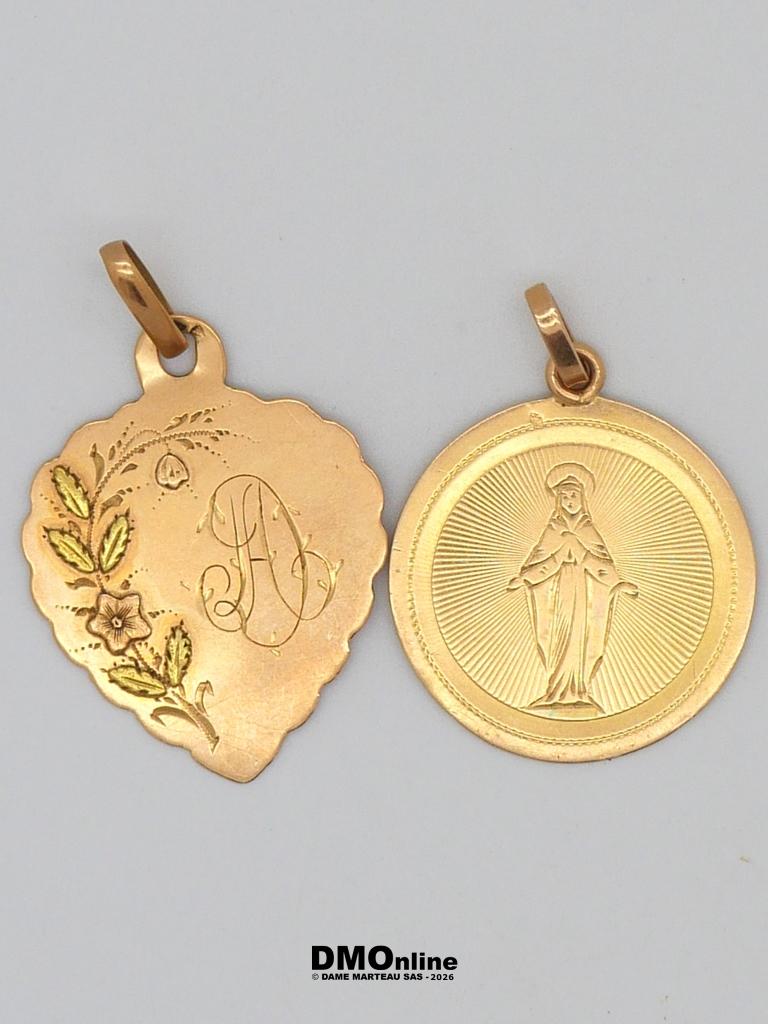 Two gold pendants on a light background: a heart-shaped charm with floral engraving and a decorative initial, and a round medallion depicting the Virgin Mary with radiating lines behind her.