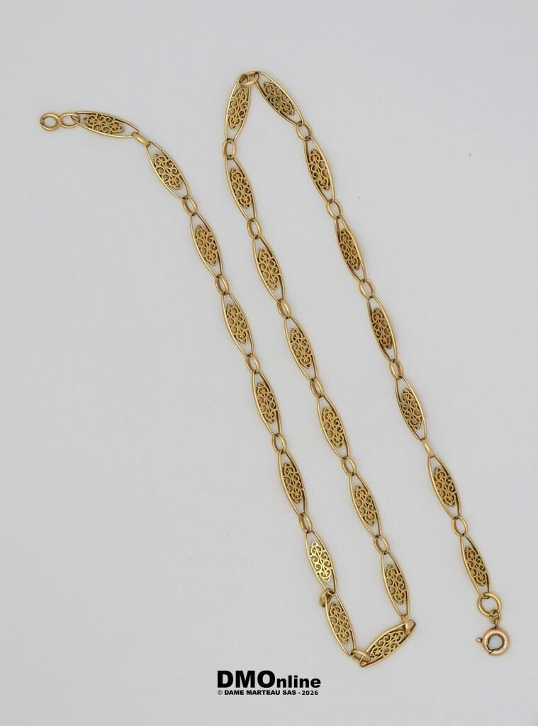 Gold chain necklace with ornate filigree oval links laid on a white surface.